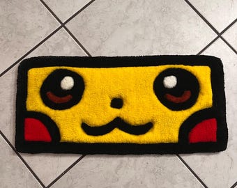 Può includere: Un tappeto rettangolare giallo con un design a forma di volto di cartone animato. Ha contorni neri, occhi neri con riflessi bianchi, macchie oculari marroni, guance rosse e una bocca nera. Il tappeto ha un bordo nero.