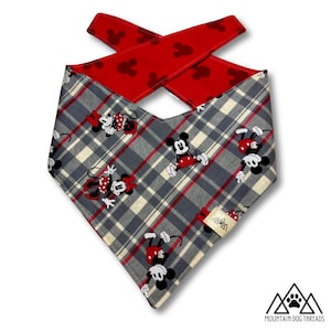 May include: A dog bandana with a gray plaid pattern and red accents. The bandana features cartoon images of Mickey and Minnie Mouse. The top layer is red with Mickey Mouse silhouettes. The bandana is from Mountain Dog Threads.