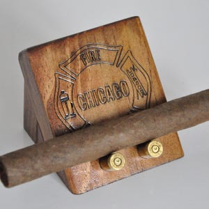 May include: Wooden cigar holder with a Chicago Fire Department logo and two bullet casings. The holder is made of dark wood and has a natural finish.
