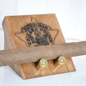 May include: Wooden cigar holder with a Chicago Police Department emblem and two bullet casings. The holder is stained a dark brown color.