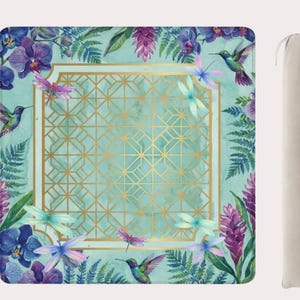 May include: A square yoga mat with a teal background, gold geometric center, and floral border. The border features purple orchids, green ferns, and hummingbirds. A beige carrying bag is included.