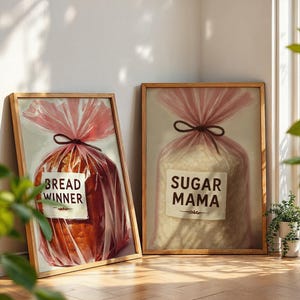 May include: Two framed prints with a food theme. One shows a loaf of bread in a pink bag with the text "BREAD WINNER". The other shows a bag of sugar with the text "SUGAR MAMA". Both are in wooden frames.