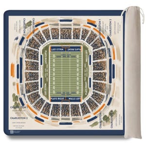 May include: A square game mat featuring a top-down illustration of a football stadium with a central field marked with yard lines and text. The design includes perimeter text labels like Charleston 1 and 2, and it comes with a beige drawstring bag.