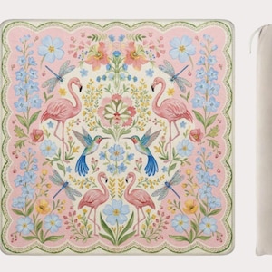 Könnte beinhalten: Eine quadratische Picknickdecke mit einem rosa Blumendesign mit Flamingos, Kolibris und Libellen. Die Decke hat einen gewellten Rand und wird mit einer beigefarbenen Tragetasche geliefert.