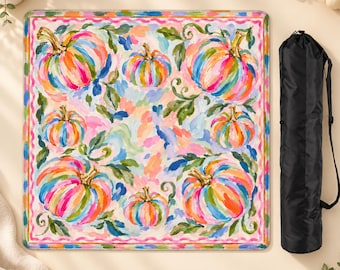 May include: A square folding table featuring a vibrant, multi-colored painted pattern of pumpkins and green leaves on a light background, framed by a pink wavy border, accompanied by a black cylindrical carrying case with a shoulder strap.