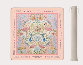 May include: A square, pink game mat with a floral and flamingo design. The mat features a central floral arrangement with pink flamingos, blue hummingbirds, and dragonflies. The edges have text that reads "Plays Right" and "Walls Left". A beige carrying bag is on the right.