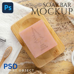Op de afbeelding: Een roze zeepblok met een boomontwerp ligt op een bamboe zeepbakje. De woorden "ADD YOUR DESIGN" staan onder de boom. De afbeelding bevat ook een tandenborstel, een handdoek en de tekst "SOAP BAR MOCKUP" en "PSD SMART OBJECT".
