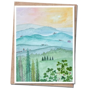 May include: Watercolor landscape art print featuring rolling hills in shades of blue and green, with a soft yellow and orange sky. The artwork includes trees, small houses, and a foreground of green foliage.