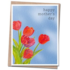 May include: A greeting card with a watercolor painting of red tulips against a light blue background. The text "happy mother's day" is written in black script. The card is set in a brown paper frame.