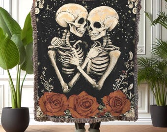 May include: A tapestry throw blanket with a dark background featuring two skeletons embracing. The skeletons are surrounded by red roses and floral designs.