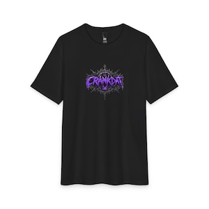 Peut inclure: Un t-shirt noir à manches courtes avec un motif graphique central. L'impression affiche le mot CRANKDAT dans une police dentelée, violette et métallique, entouré d'un emblème sombre, circulaire et épineux aux lignes complexes.