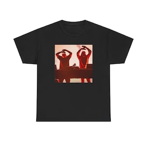 May include: Black t-shirt with a graphic of two people in red silhouettes, standing in front of a DJ setup.