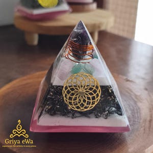 Può includere: Un'opera d'arte in resina trasparente a forma di piramide con base rosa, contenente cristalli, un design in metallo color oro e filo di rame. La piramide ha un design a strati con vari colori e trame.
