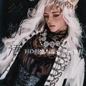 Puede incluir: Una muñeca con pelo largo blanco y una corona enjoyada aparece en la portada de un libro. La muñeca lleva un atuendo blanco y negro con joyas intrincadas. El título del libro está en caracteres chinos, con el texto "Tutorial de fabricación de pelucas y globos oculares BJD".