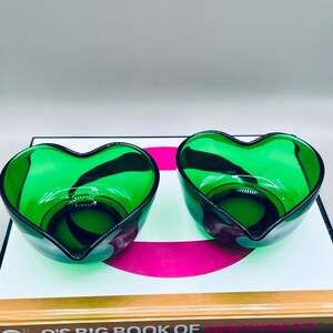 Puede incluir: Dos cuencos de vidrio en forma de coraz&oacute;n. Los cuencos son de un verde vibrante con un acento verde oscuro y un borde negro. Los cuencos est&aacute;n sobre una superficie blanca con una franja rosa.