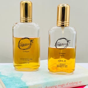 May include: Two clear glass Stetson cologne bottles with gold-colored caps. One bottle is labeled "Cologne" and the other "Cologne Spray". Both bottles contain amber-colored liquid. The bottles are on a book titled "the life-changing magic of tidying up".