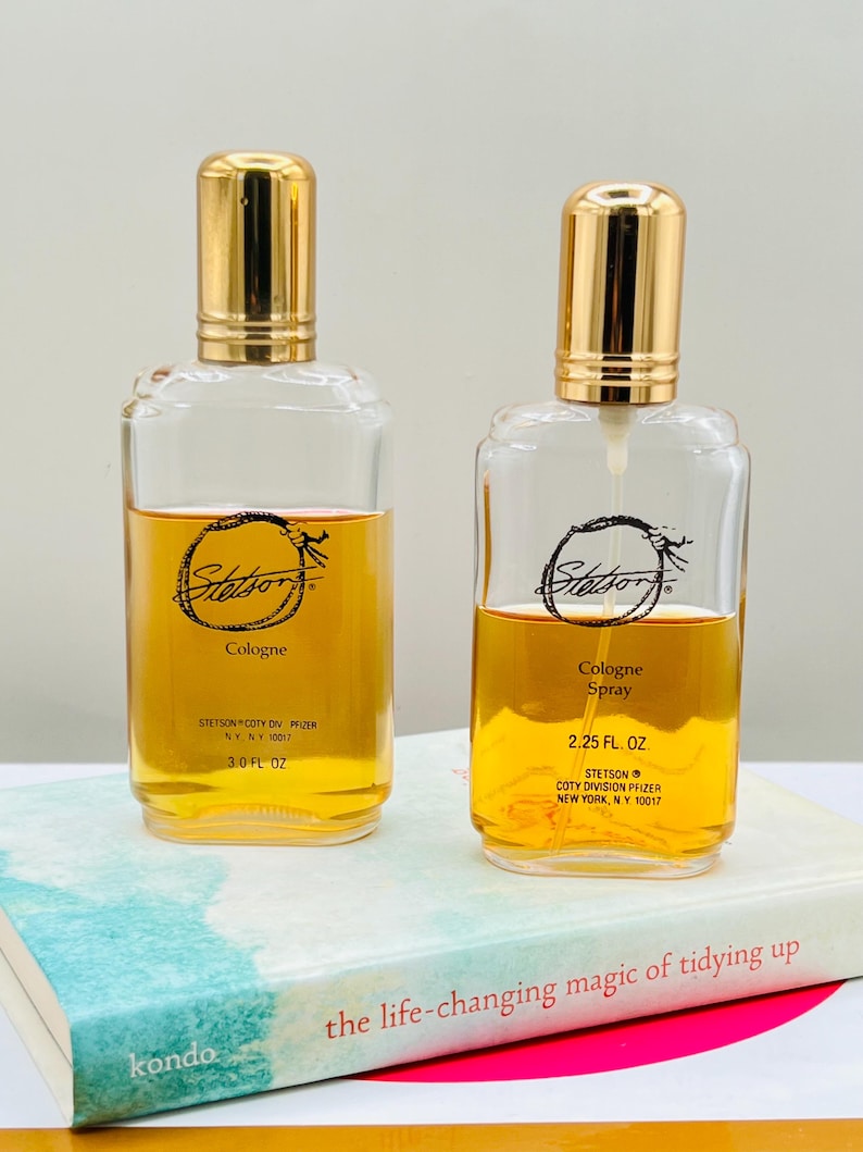 May include: Two clear glass Stetson cologne bottles with gold-colored caps. One bottle is labeled "Cologne" and the other "Cologne Spray". Both bottles contain amber-colored liquid. The bottles are on a book titled "the life-changing magic of tidying up".