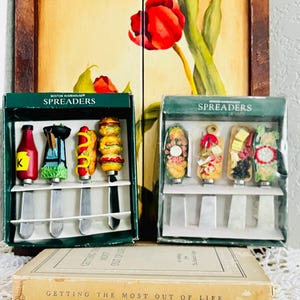 Peut inclure: Deux coffrets de tartineurs Boston Warehouse. La boîte de gauche contient quatre tartineurs avec des manches en forme de bouteille de ketchup, de barbecue, de hot-dog et de burger. La boîte de droite présente quatre tartineurs à motifs alimentaires.