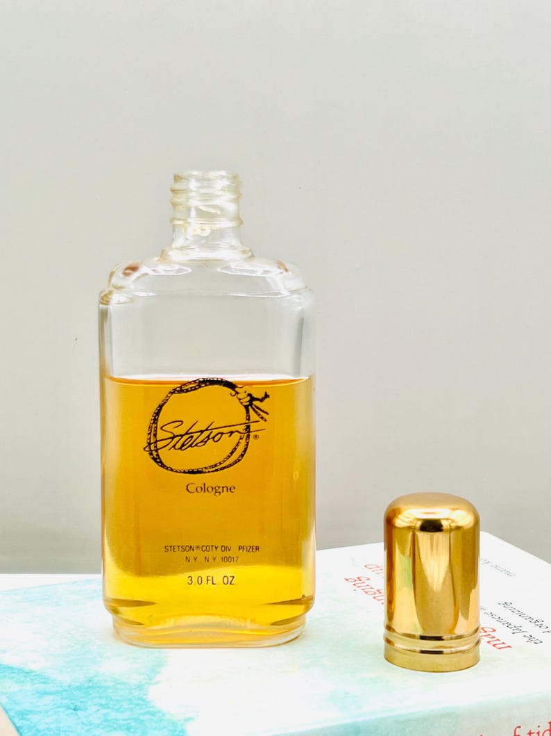 May include: A clear glass bottle of Stetson cologne with a gold cap. The bottle contains a golden-colored liquid and has the Stetson logo and text printed on the front. The bottle is 3.0 fl oz.
