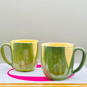 May include: A white ceramic mug with a black handle and the text "But First, Coffee" in a bold, black font. The mug is set against a blurred background, suggesting a cozy setting.