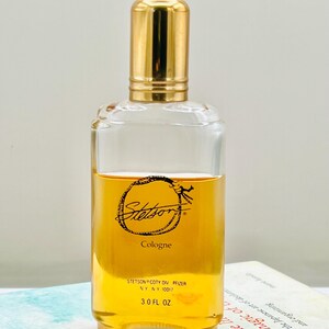 May include: A clear glass cologne bottle with a gold-colored cap. The bottle contains a golden-amber liquid and features the "Stetson" logo and "Cologne" text. The bottle is labeled "3.0 FL OZ".