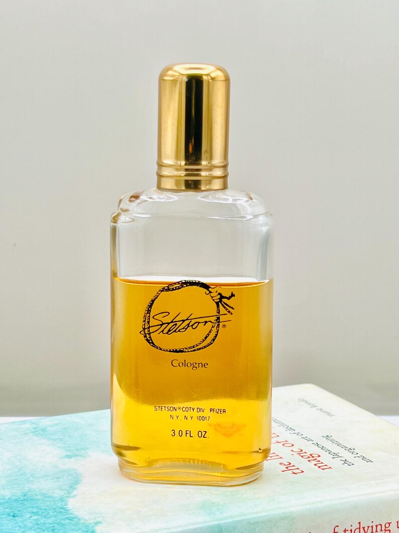 May include: A clear glass cologne bottle with a gold-colored cap. The bottle contains a golden-amber liquid and features the "Stetson" logo and "Cologne" text. The bottle is labeled "3.0 FL OZ".