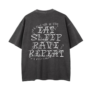 Puede incluir: Una camiseta negra de manga corta con un aspecto desgastado. La parte posterior de la camiseta tiene un gráfico blanco que dice "Eat Sleep Rave Repeat" en una fuente estilizada.