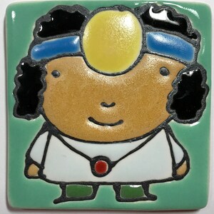 May include: A hand-painted ceramic tile featuring a cartoon doctor with a stethoscope, a white coat, and a blue headband. The doctor has brown skin, black hair, and a yellow eye patch.