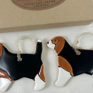 May include: Two ceramic beagle dog ornaments with black, brown, and white paint. Each ornament has a gold string attached for hanging.