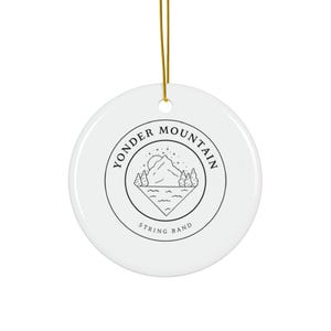 May include: A white ceramic disc ornament with a gold hanging string. The design features a black and white mountain scene and the text "Yonder Mountain String Band" in a circular arrangement.