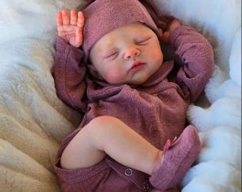May include: A sleeping baby wearing a mauve-colored outfit, including a hooded onesie, hat, and booties. The baby is lying on a soft, white, fluffy blanket. The baby's eyes are closed, and its arms are raised.