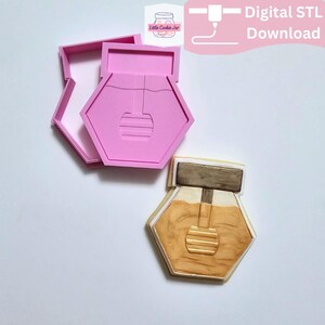 May include: A pink plastic cookie cutter shaped like a honey pot with a dipper, accompanied by a decorated cookie featuring a brown lid, a golden honey-filled body, and a honey dipper design. The image includes the text Digital STL Download.