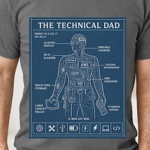 May include: A gray t-shirt featuring a blue blueprint design labeled "THE TECHNICAL DAD." The blueprint depicts a human figure with technical components like a Wi-Fi scanner, portable charger, and TV remote control. The shirt has a crew neck and short sleeves.