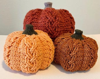May include: Three crocheted pumpkins in different sizes and colors. The largest pumpkin is a deep red, the medium pumpkin is a light orange, and the smallest pumpkin is a dark orange.