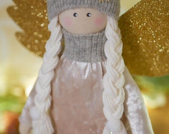May include: A handmade angel doll with a gray knit hat featuring a gold snowflake. The doll has long white braided hair, rosy cheeks, and wears a pink velvet dress with gold trim. Gold glitter wings are visible.