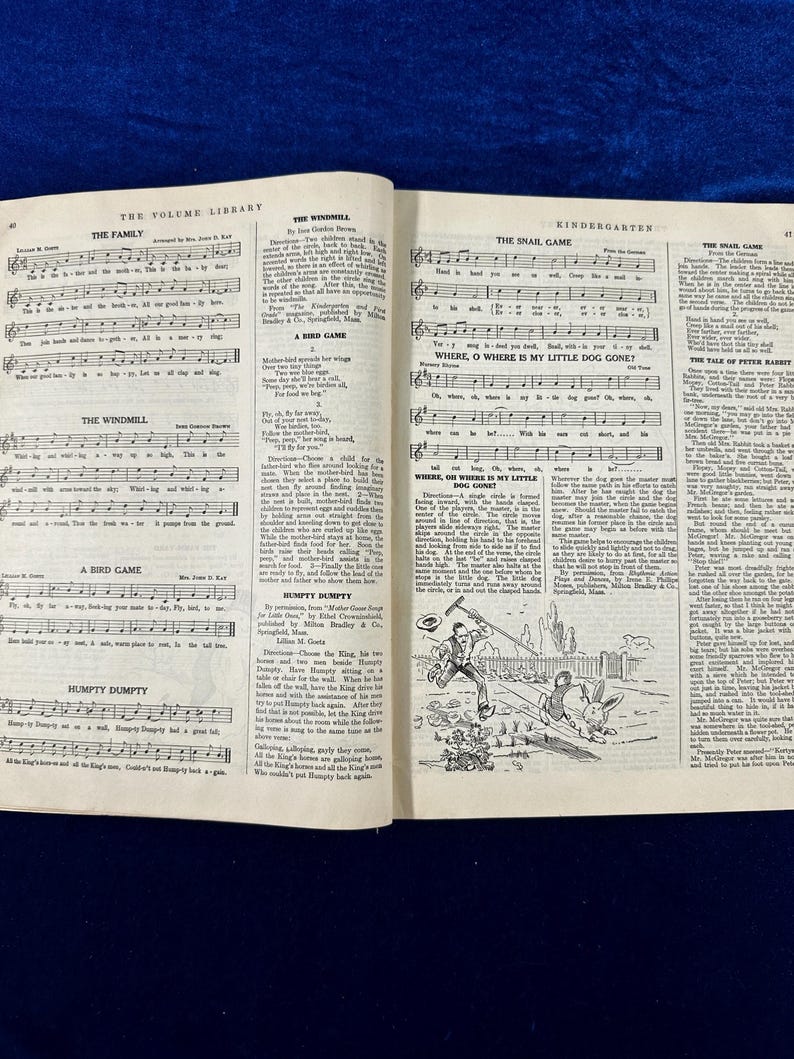 May include: A vintage book with a black and white illustration of a snail on the cover. The book is open to a page with sheet music for children's songs. The songs include "The Family", "The Windmill", "A Bird Game", "Humpty Dumpty", "The Snail Game", "Where, O Where Is My Little Dog Gone?", "Where, Oh Where Is My Little Dog Gone?", "The Tale of Peter Rabbit", and "The Wild Game".