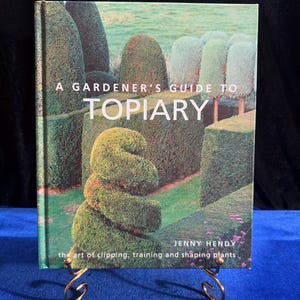 May include: A green book titled "A Gardener's Guide to Topiary" by Jenny Hendy. The book cover features a photo of a topiary garden with a variety of shapes and sizes of trimmed shrubs.
