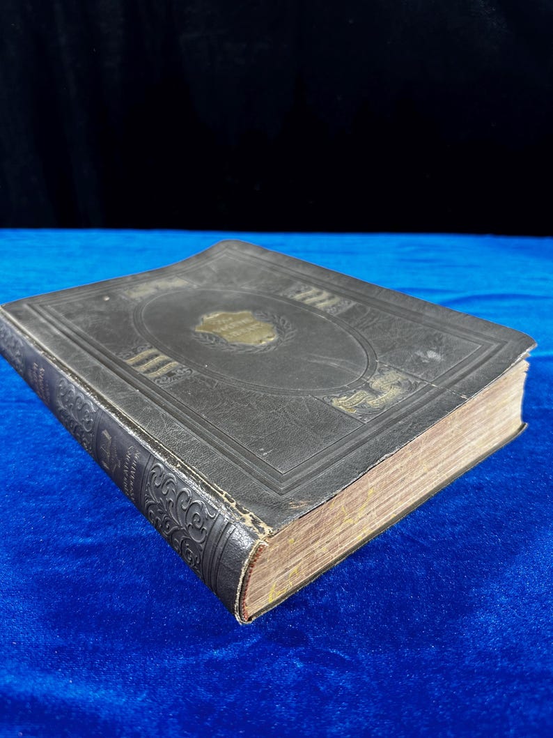 May include: A vintage, dark brown leather-bound book with gold accents and intricate designs on the cover. The book is closed and lying on a blue surface.