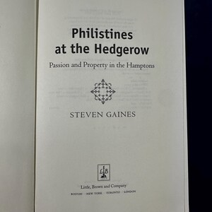 May include: A book cover with the title "Philistines at the Hedgerow: Passion and Property in the Hamptons" by Steven Gaines. The cover is white with black text and a decorative design.