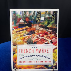 May include: A white cookbook with a colorful image of a French market on the cover. The title is "The French Market: More Recipes from a French Kitchen" by Joanne Harris & Fran Warde.
