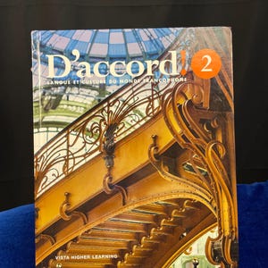 May include: A book titled "D'accord! 2" with a yellow and orange cover featuring a photo of a wrought iron staircase with a glass ceiling. The book's subtitle is "Langue et Culture du Monde Francophone" and the bottom of the cover reads "Vista Higher Learning".