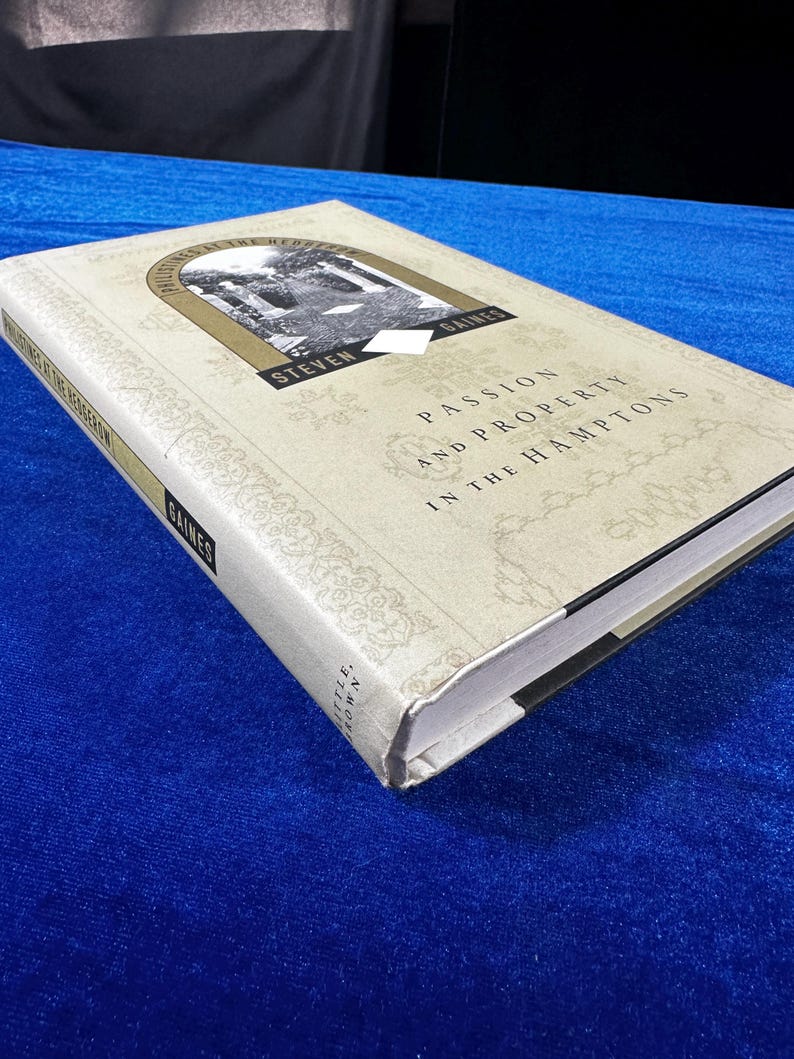 May include: A white hardcover book with the title "Passion and Property in the Hamptons" by Steven Gaines. The book cover features a black and white photograph of a building with columns.