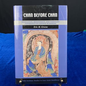 May include: A book titled "CHAN BEFORE CHAN" with text about meditation and Chinese Buddhism. The cover is a light purple with black text and a colorful illustration of a figure in a seated position. The author's name is Eric M. Greene.