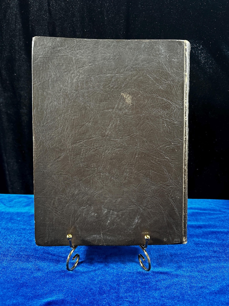 May include: A brown leather-bound book with a textured cover. The book is standing on a gold metal stand.