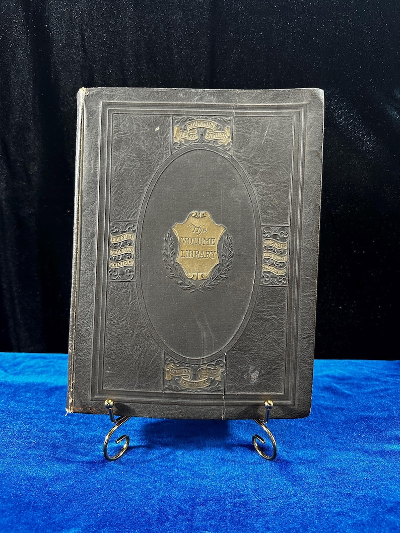 May include: A dark gray leather-bound book with gold lettering and decorative accents. The title "The Volume Library" is embossed on the front cover.