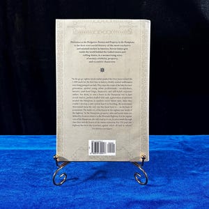 May include: A beige book cover with a black and white image of a star on the front. The book title is "Philistines at the Hedgerow: Passion and Property in the Hamptons" and the author is Steven Gaines. The back cover has a blurb about the book and a barcode.
