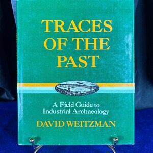 May include: A green book titled "TRACES OF THE PAST" with yellow lettering. The book cover features an illustration of a bridge and the text "A Field Guide to Industrial Archaeology" and the author's name, David Weitzman.
