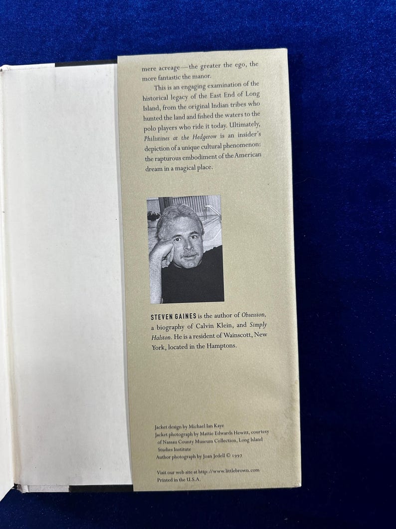 May include: A book cover with a photo of a man with a beard and glasses. The book title is "Philistines at the Hedgerow" and the author is Steven Gaines. The back cover text describes the book as an engaging examination of the historical legacy of the East End of Long Island.