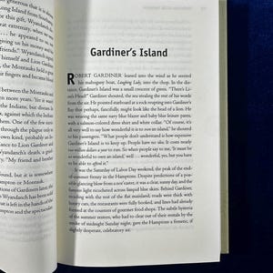 May include: A book page with a black and white photo of a boat on the water. The text on the page reads "Gardiner's Island" and "Robert Gardiner leaned into the wind as he steered his mahogany boat, Laughing Lady, into the chop."