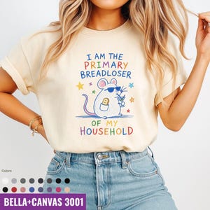 May include: Cream-colored t-shirt with the text "I AM THE PRIMARY BREADLOSER OF MY HOUSEHOLD." A cartoon mouse wearing sunglasses and holding a cocktail is featured in the center. The shirt is made of Bella+Canvas 3001 material.